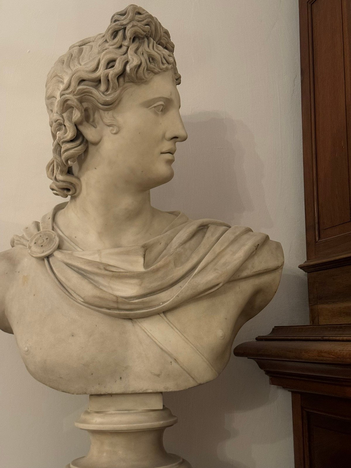 Busto in marmo di Apollo accanto a una credenza intagliata