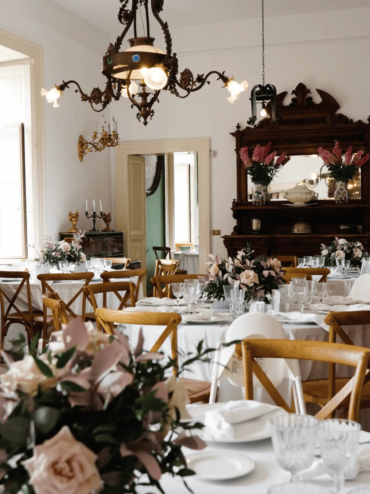 Tavoli allestiti con rose e cristalli sotto il lampadario d'epoca