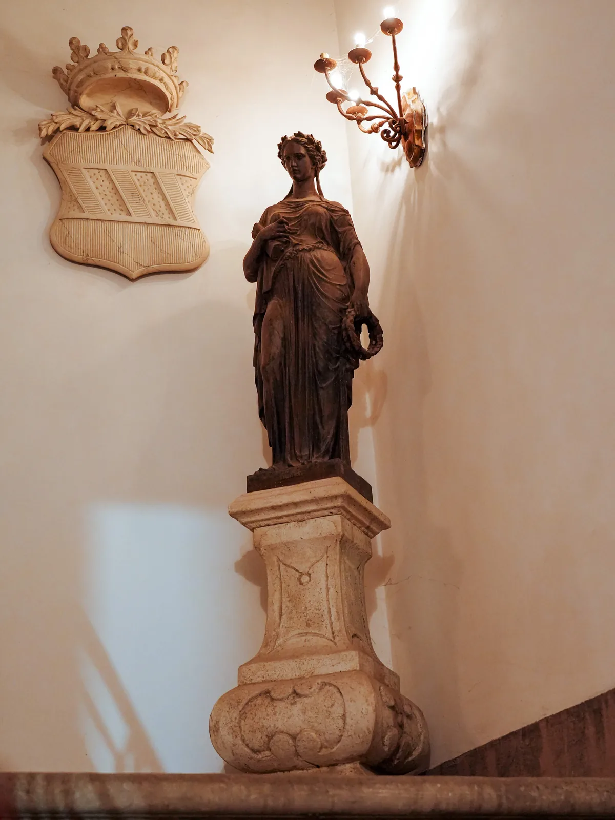 Statua in marmo su piedistallo accanto a un'applique in ferro battuto